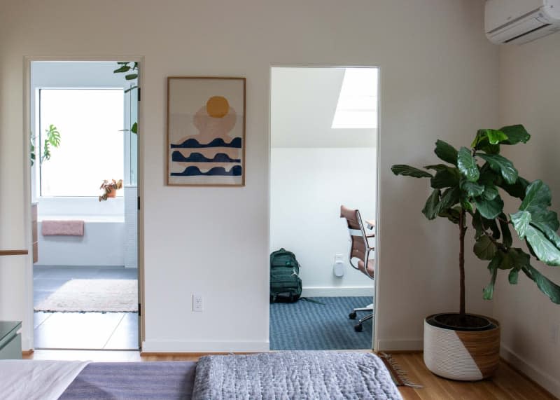 View of of home office and bathroom from hallway with potted plant.