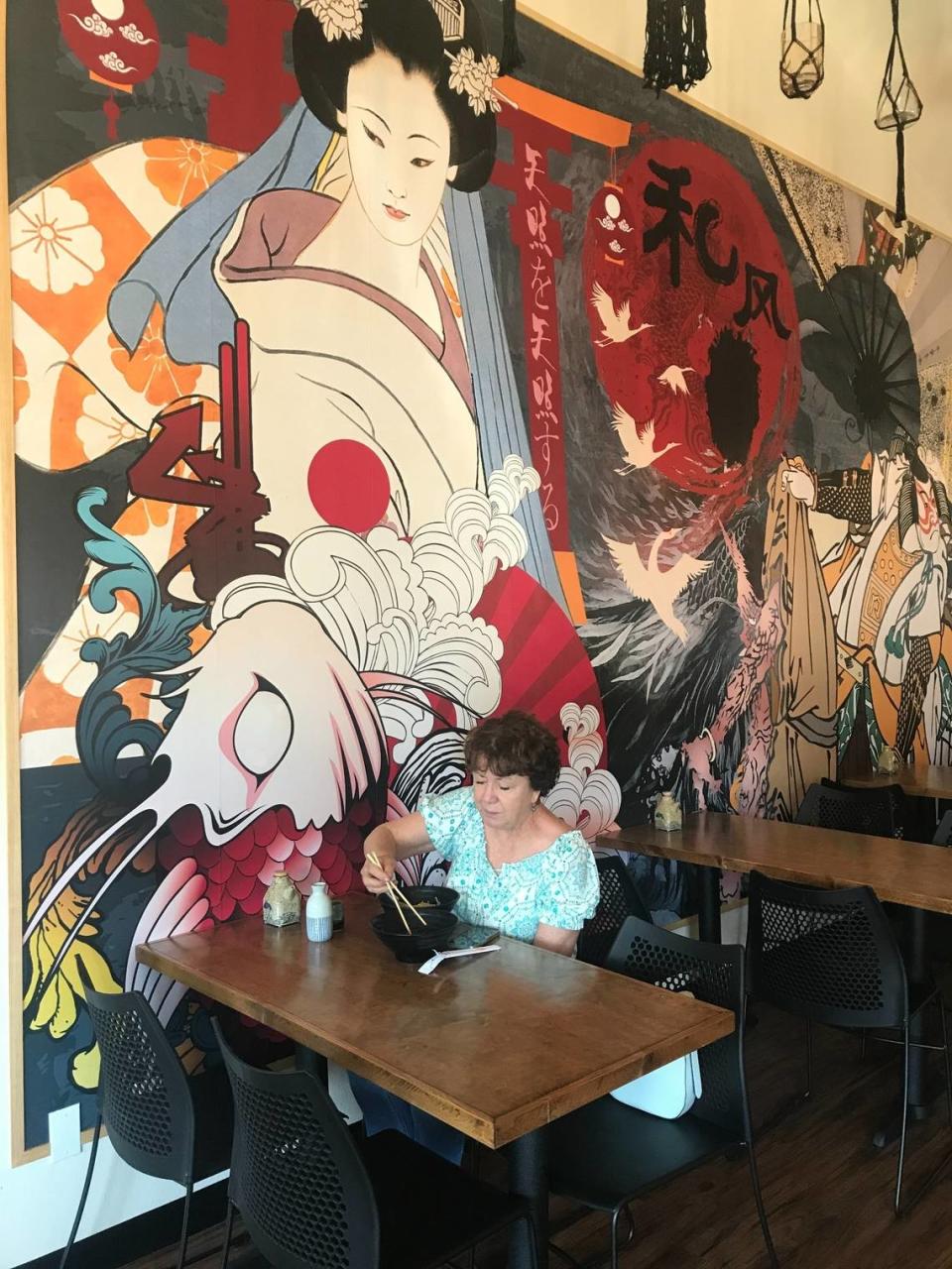 Regular Chowa Bowl customer Diane Toman of Cayucos dines on ramen and skewers of grilled filet mignon on Wednesday, May 8, 2024. Her backdrop is part of a 17-foot-wide mural on silk.