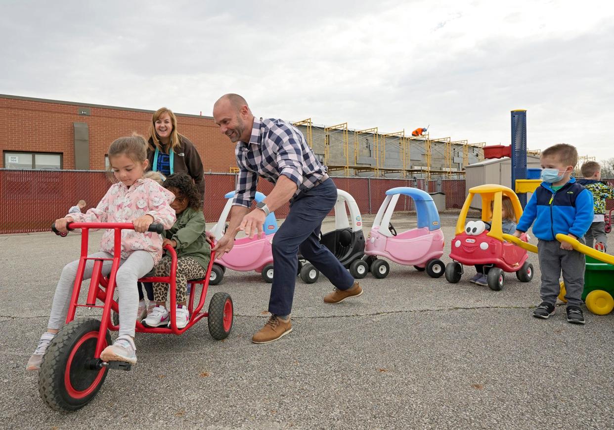 Principal Brian Hart gives children on a bike a push at Hilliard City Schools Preschool on April 22. An expansion to the school, which is to add eight classrooms and space for 60 more students, is shown in the background.