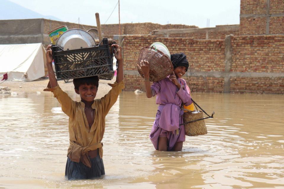 Niños cargan artículos domésticos mientras atraviesan un área inundada después de una lluvia monzónica en Quetta (AFP vía Getty Images)