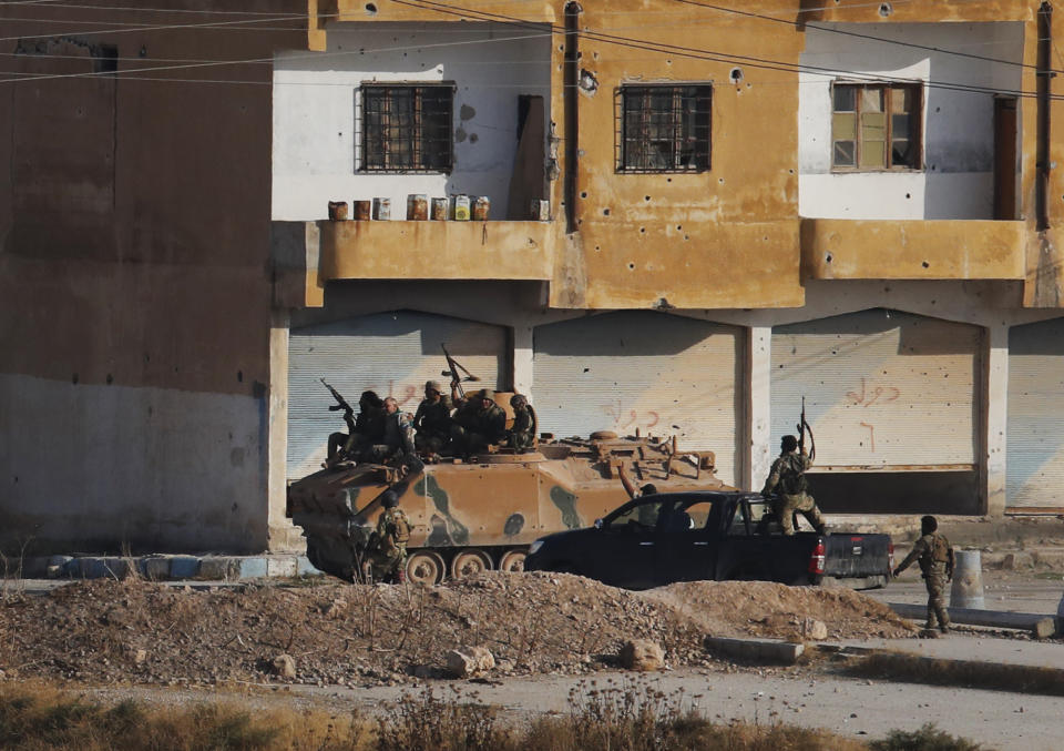 In this photo taken from the Turkish side of the border between Turkey and Syria, in Akcakale, Sanliurfa province, southeastern Turkey, Turkish-backed Syrian opposition fighters advance with theirs armoured personnel carrier in Tel Abyad, Syria, Sunday, Oct. 13, 2019. Fighting continued into the afternoon in Tel Abyad, where smoke could be seen rising from several points in the town. (AP Photo/Lefteris Pitarakis)