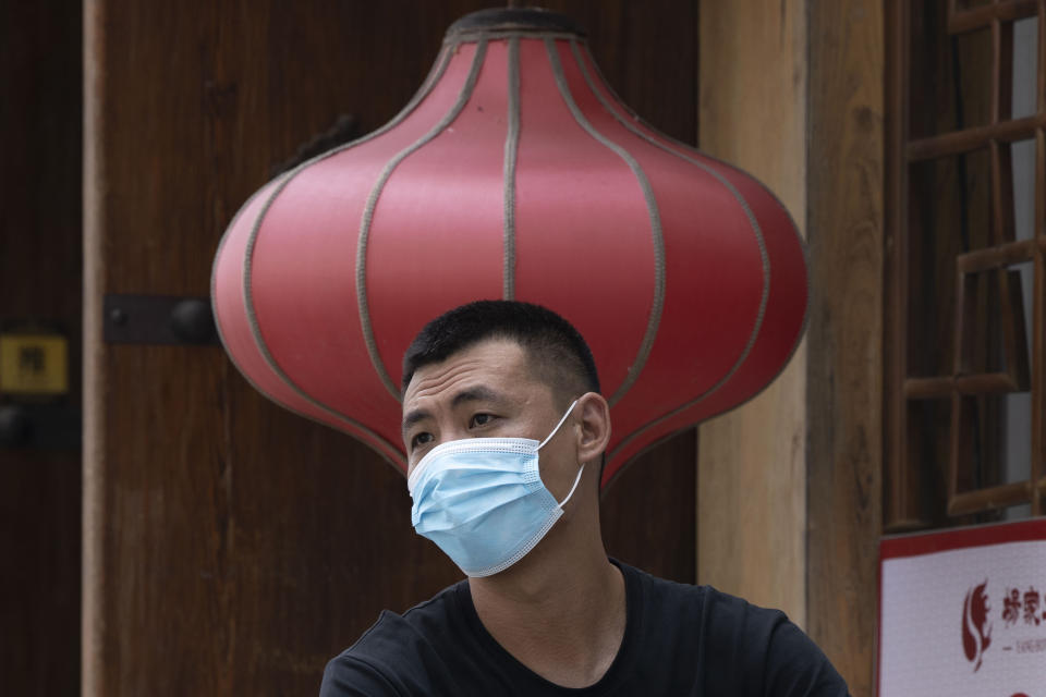 A man wearing a mask to curb the spread of the coronavirus sits near a red lantern outside a restaurant in Beijing Monday, July 13, 2020. China reported eight new cases, all of them brought from outside the country, as domestic community infections fall to near zero. (AP Photo/Ng Han Guan)