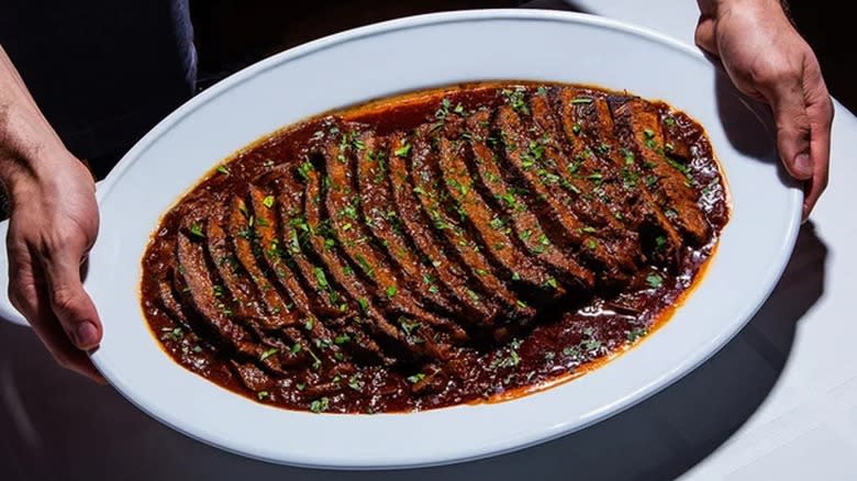 Hands holding a platter of braised brisket