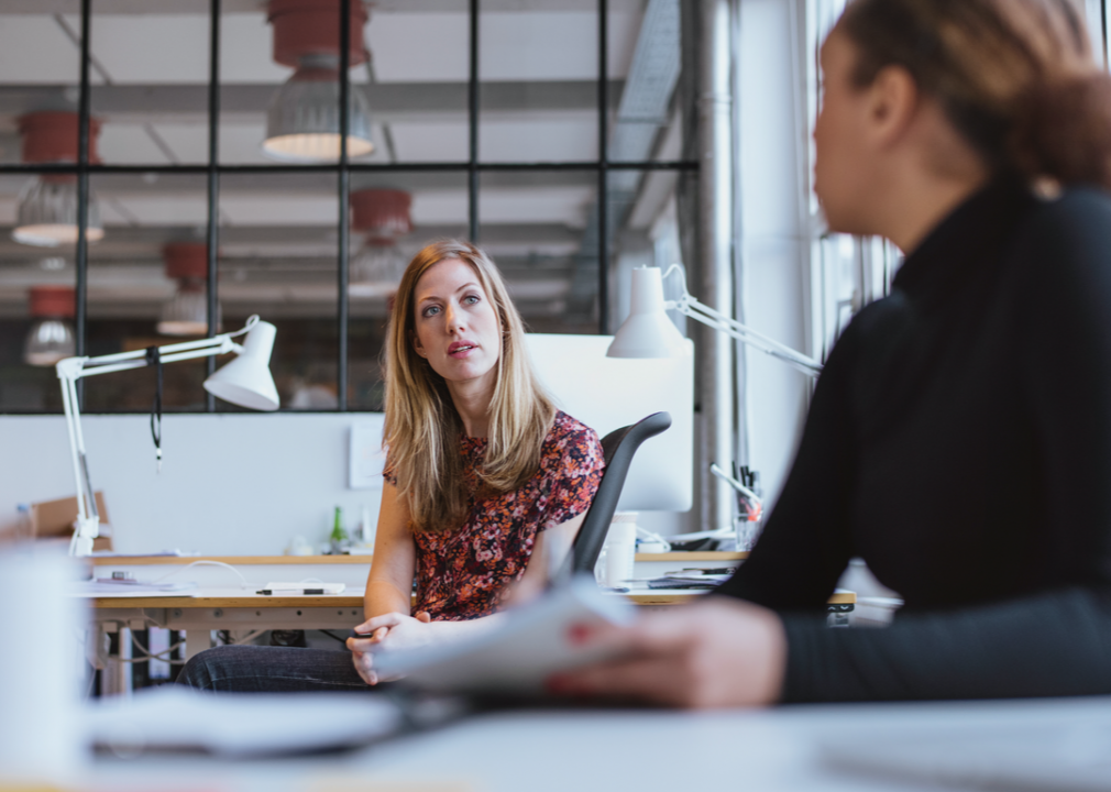 Two people sitting at their desks talking.