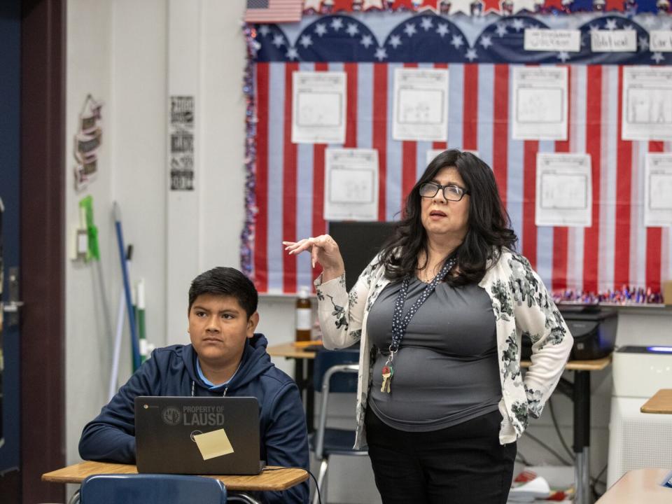 Teacher Lorraine Escalante stands near a seated student