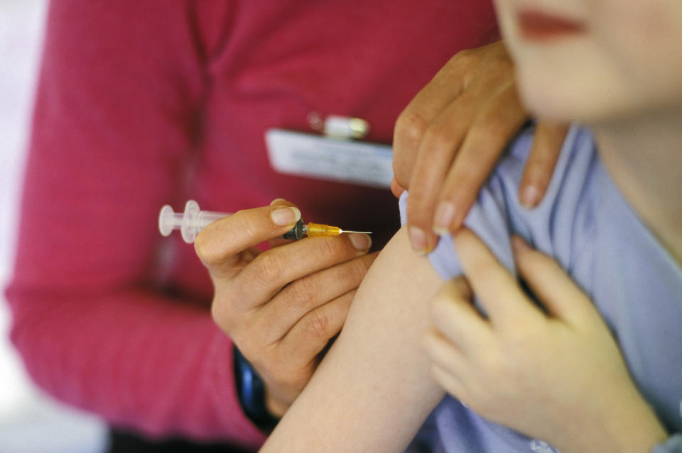 A child about to be given the MMR (mumps, measles, rubella) vaccination into their arm by a surgery nurse with a hypodermic syringe, England, UK.