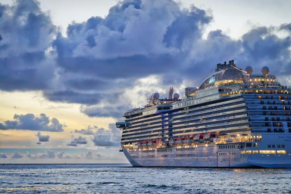 Learn more about the specifics of long term cruises and a few pros and cons.
Pictured: a large cruise ship lit up at night cruising along in the evening 