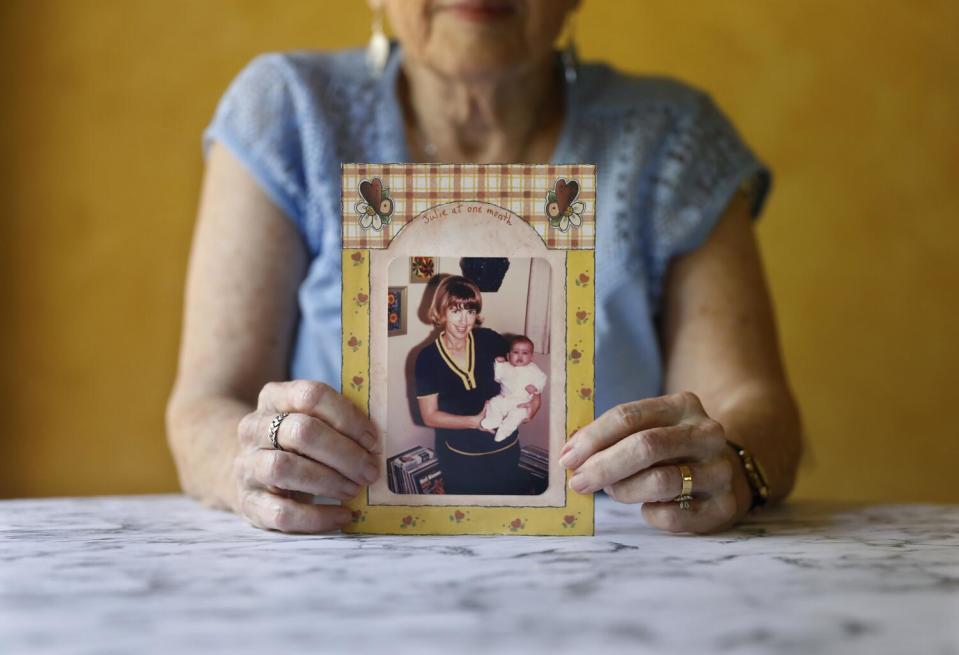 A woman holds a photograph of herself holding a baby.