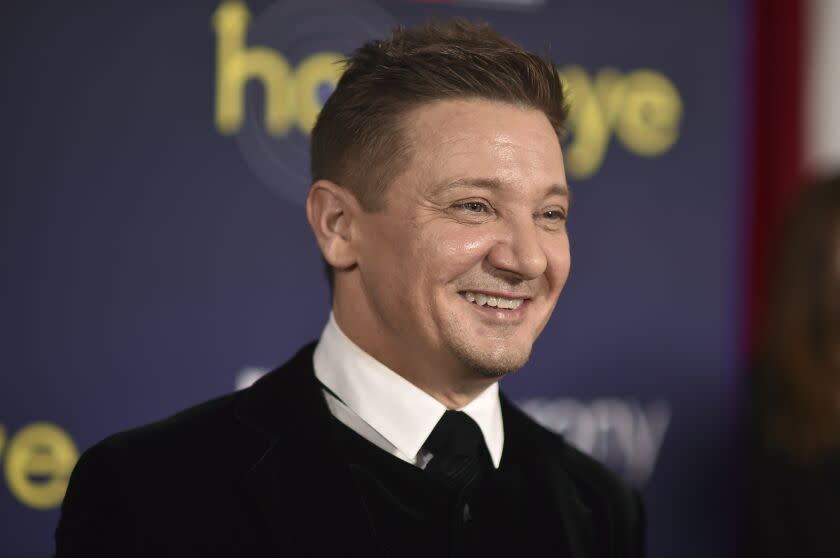 A man with short brown hair smiling in a black suit and tie