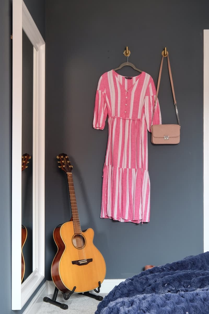 slate gray walls, white framed full length mirror, pink and white striped dress hanging next to purse and guitar on stand in corner