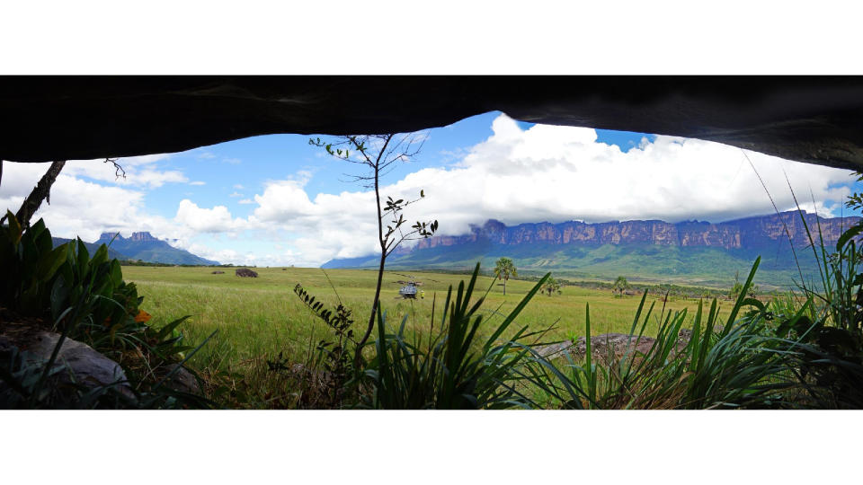 A panoramic view from the cave over a grassy plain with rocky mesas