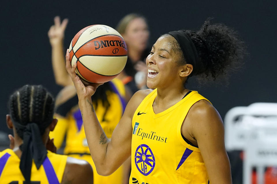 Candace Parker in a yellow Sparks jersey holds the basketball up. 