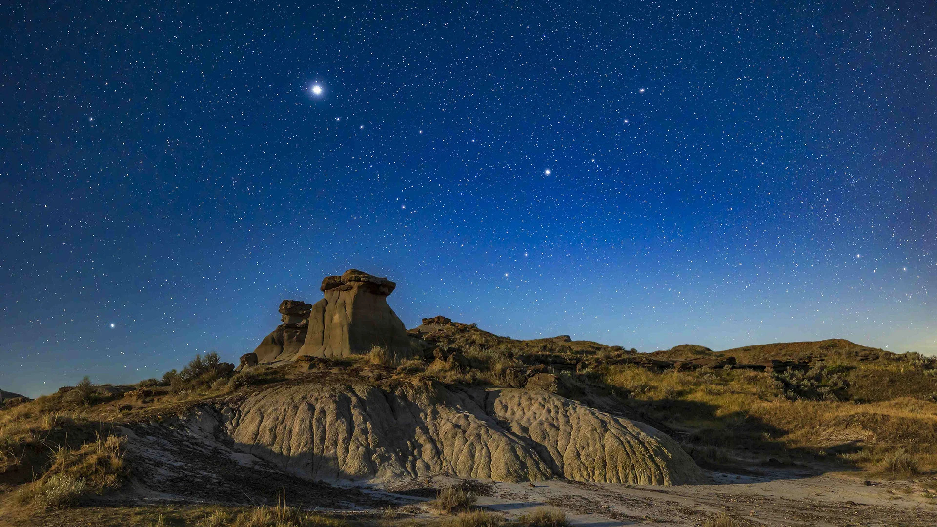 Jupiter (bright at left) and Saturn (dimmer at centre) over hoodoo formations at Dinosaur Provincial Park, Alberta, August 29/30, 2021, with the foreground illuminated by moonlight from the rising last quarter Moon. The planets are in or near the constellation of Capricornus framed at centre. This is a blend of two images: a single tracked 1-minute exposure for the sky at f/2.8 and ISO 800 plus a single untracked 3-minute exposure for the ground at f/4 and ISO 800, both with the Canon 15-35mm RF lens at 29mm and Canon R6 camera on the Star Adventurer Mini tracker. I added a mild Orton effect with Luminar AI. Long Exposure Noise Reduction applied to the ground image in camera. (Photo by: Alan Dyer/VW Pics/Universal Images Group via Getty Images). 