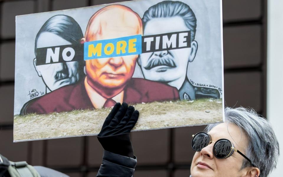 A woman holding a placard depicting Adolf Hitler, Putin and Joseph Stalin protests in front of the Russian embassy in Moldova