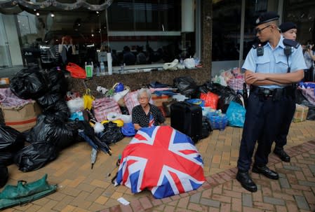 A police officer looks at a protester sitting amongst umbrellas, bags and other items that were salvaged following protest in Hong Kong