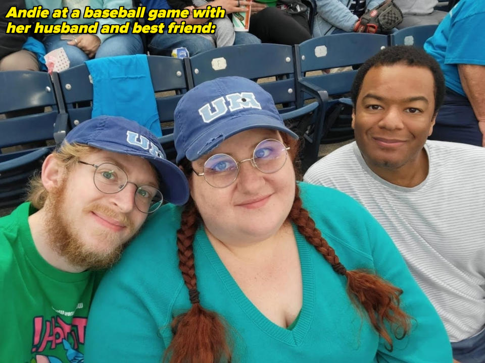 Group selfie at an event: three people, two wearing baseball caps with "UM" and glasses, all smiling and sitting in a stadium
