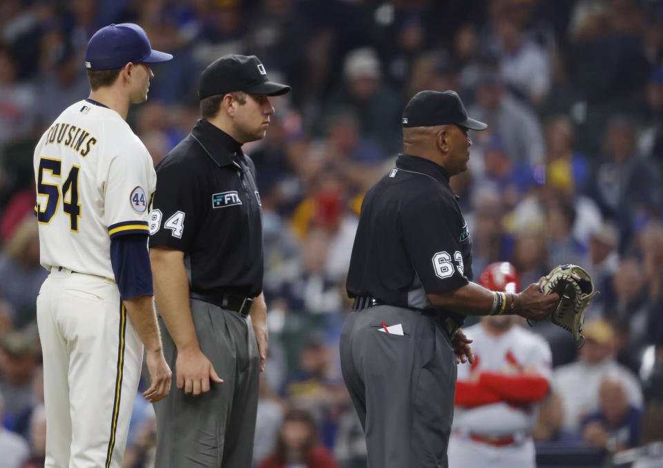 Umpire Lazaro Diaz (63) removes the glove of Milwaukee Brewers pitcher Jake Cousins (54) during the seventh inning of a baseball game against the St. Louis Cardinals, Thursday, Sept. 23, 2021, in Milwaukee. (AP Photo/Jeffrey Phelps)