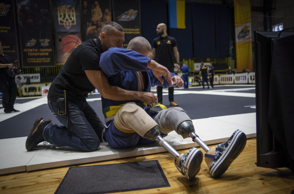 26-year-old Vasyl Oksyntiuk, right, Ukrainian war veteran receives help of tying the belt of his kimono during Ukrainian national competition of jiu jitsu in Kyiv, Ukraine, Sunday, Oct. 29, 2023. More than 20,000 people in the Ukraine have lost limbs from injuries since the start of the Russian war, many of them soldiers. Some of them have learned to deal with their psychological trauma by practicing a form of Brazilian jiu-jitsu. (AP Photo/Hanna Arhirova)
