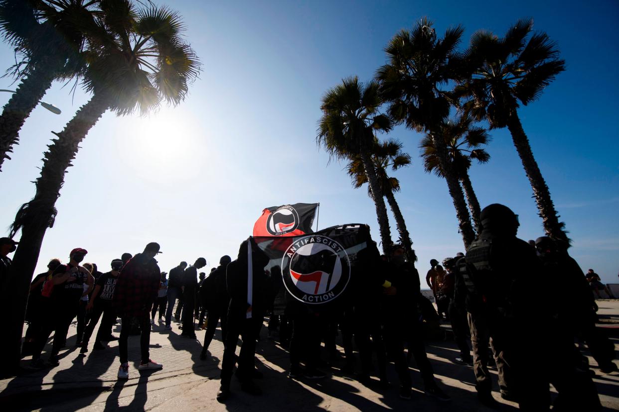 Counter-protesters, some carrying ANTIFA flags, stand beneath palm trees on the beach awaiting to confront demonstrators for a "Patriot March" demonstration in support of US President Donald Trump on Jan. 9, 2021, in the Pacific Beach neighborhood of San Diego, California.