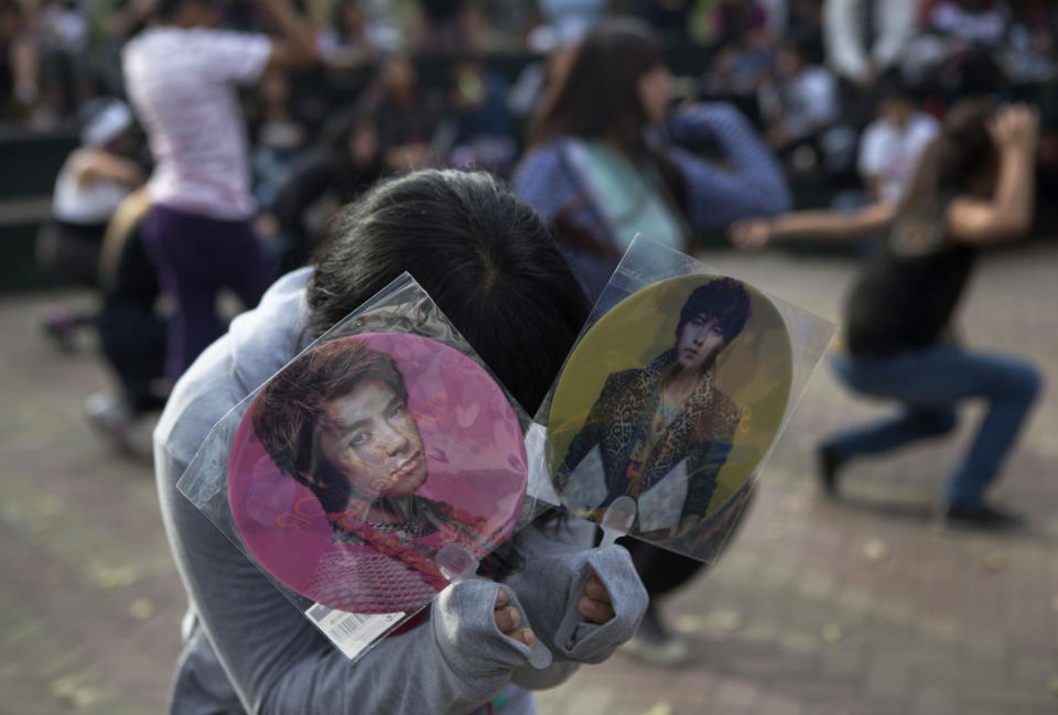 In this May 18, 2013 photo, a member of a fan club for South Korean singer Kim Kyun Jong shows his photographs of the singer as his friends dance in the background in Ramon Castilla park where fans gather in Lima, Peru. Joong was met by thousands of fans when he arrived at the airport in Peru's capital in February this year. (AP Photo/Martin Mejia)