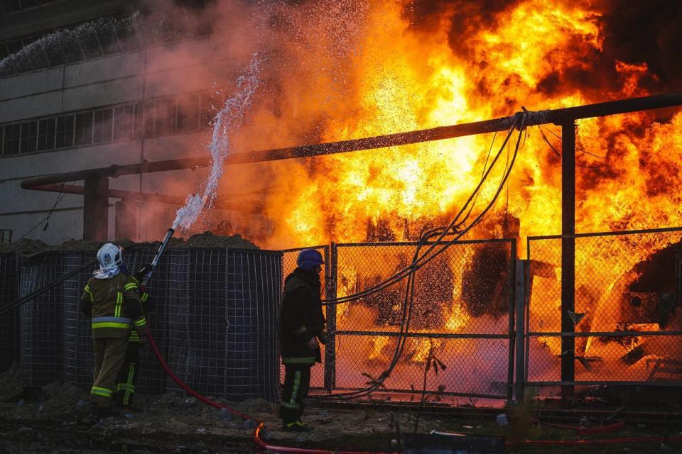 A man in a helmet watches a blaze as a colleague trains a hose on it.