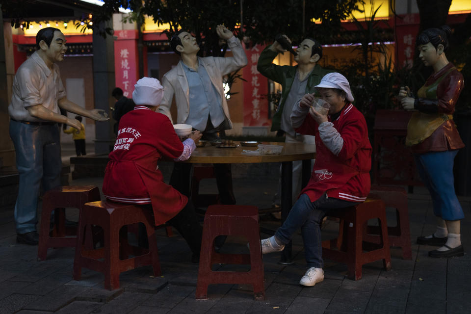 Restaurant workers eat during a break next to sculptures depicting a boisterous dining crowd in Wuhan on Sunday, Oct. 18, 2020. (AP Photo/Ng Han Guan)