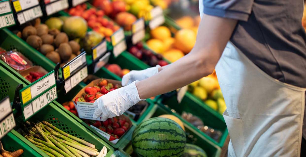 A grocery story worker places boxes of strawberries among other fruits and vegetables at the store. ies, have higher amounts of pesticides than others. But how harmful is it? (Photo: Getty Images)