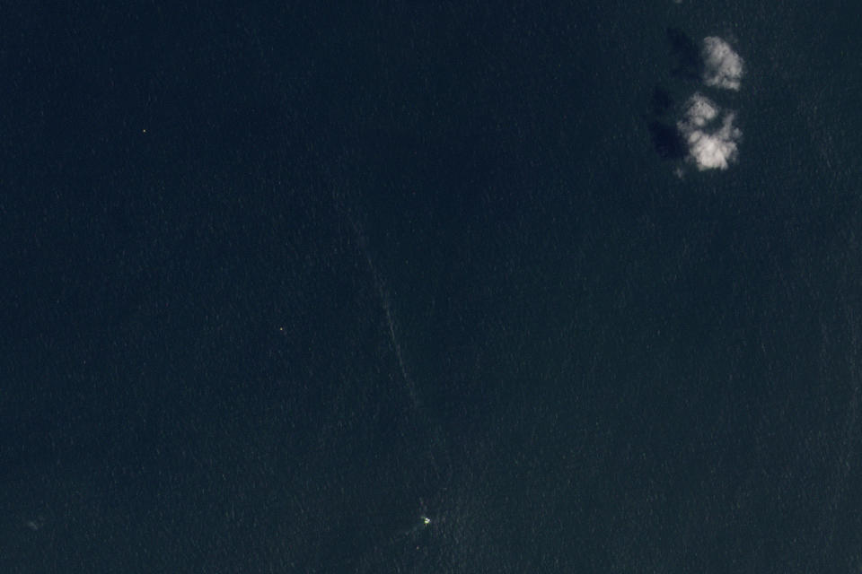 This satellite image from Planet Labs shows an oil spill still leaking from the wreckage of the Trinity Spirit ship, bottom center, with clouds at upper right, on Sept. 30, 2023, after an explosion occurred aboard the ship in February 2022. The ship was used to store and refine large quantities of oil extracted from the ocean floor and moored 15 miles off the coast of Nigeria. The vessel was carrying 40,000 barrels of oil. (Planet Labs via AP)