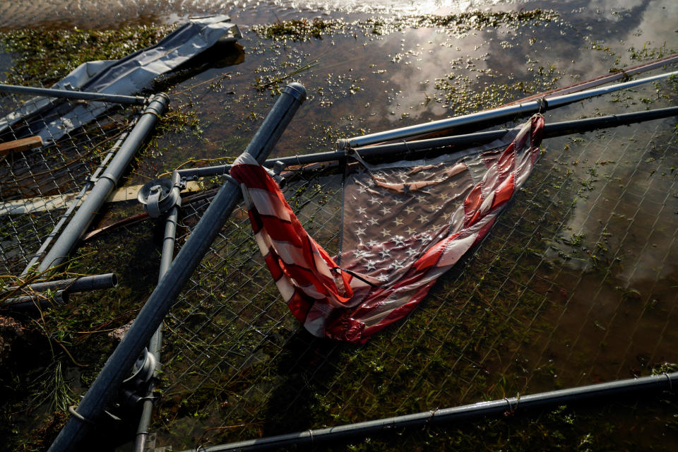 An American flag and a destroyed chain-link fence in floodwater.