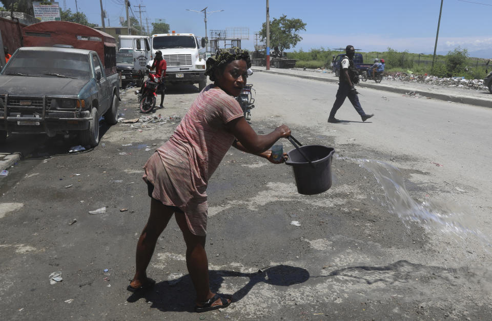 A woman covers the side of the street with water to keep dirt from kicking up, as police patrol near the airport in Port-au-Prince, Haiti, Friday, May 24, 2024. (AP Photo/Odelyn Joseph)