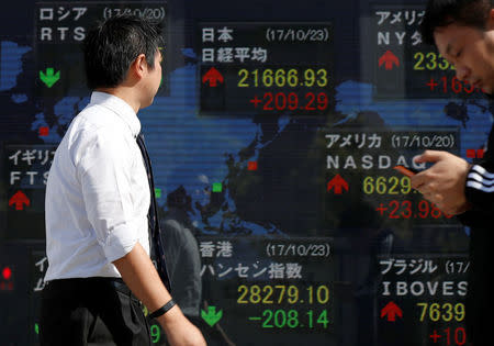 Passersby walk past an electronic board showing market indices outside a brokerage in Tokyo, Japan, October 23, 2017. REUTERS/Issei Kato