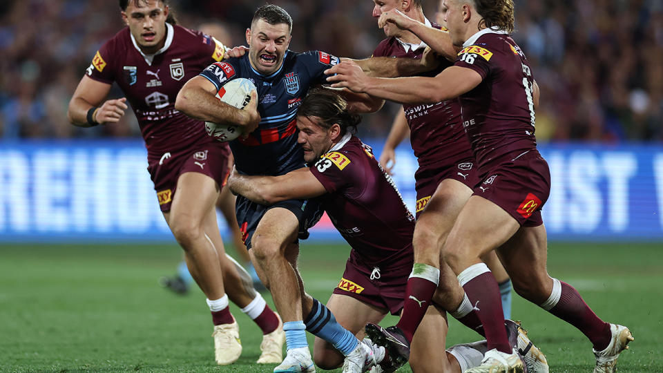 NSW player James Tedesco is tackled by several Queensland opponents.