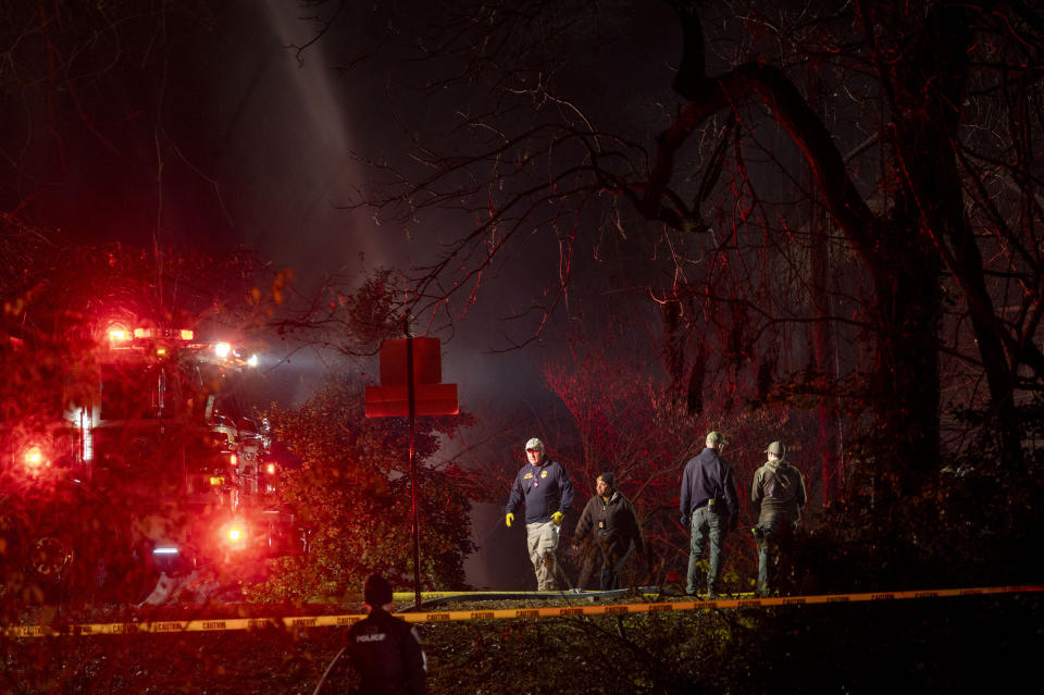 Fire and police officials walk around the scene of a house explosion as an Arlington County Fire Department ladder truck sprays water down on the remains of the building on Monday, Dec. 4, 2023, in Arlington, Va. (AP Photo/Kevin Wolf)