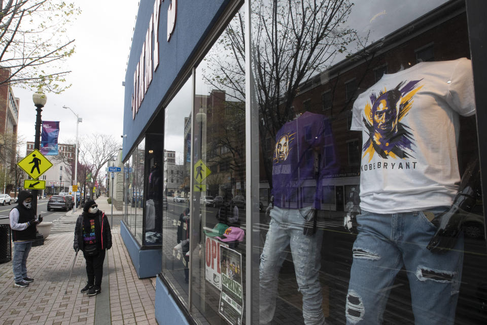 FILE- In this April 27, 2020 file photo, a couple of residents wearing face masks to protect from the coronavirus window shop at a closed clothing store on Main Street in downtown in Bridgeport, Conn. Although New York City is the epicenter of the coronavirus outbreak, the virus has significantly impacted cities and towns in New Jersey and Connecticut. (AP Photo/Mary Altaffer, File)