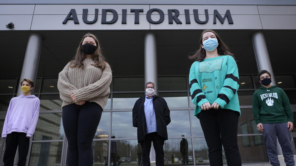 While wearing protective masks due to the COVID-19 outbreak, Jim Howard, a drama teacher at Westwood, Mass., High School, center, poses with his student actors outside the school's auditorium after working on their virtual performance of Shakespeare's "Romeo and Juliet," Monday, Nov. 16, 2020, in Westwood. The production, which would usually be presented onstage, shifted to a virtual audience due to the pandemic. From left are Ryan Kaplan, who portrays the friar, Lucy Vitali, who portrays Juliet, Howard, Cassidy Hall, who portrays the nurse, and Alex Mansour, who portrays Romeo. (AP Photo/Charles Krupa)