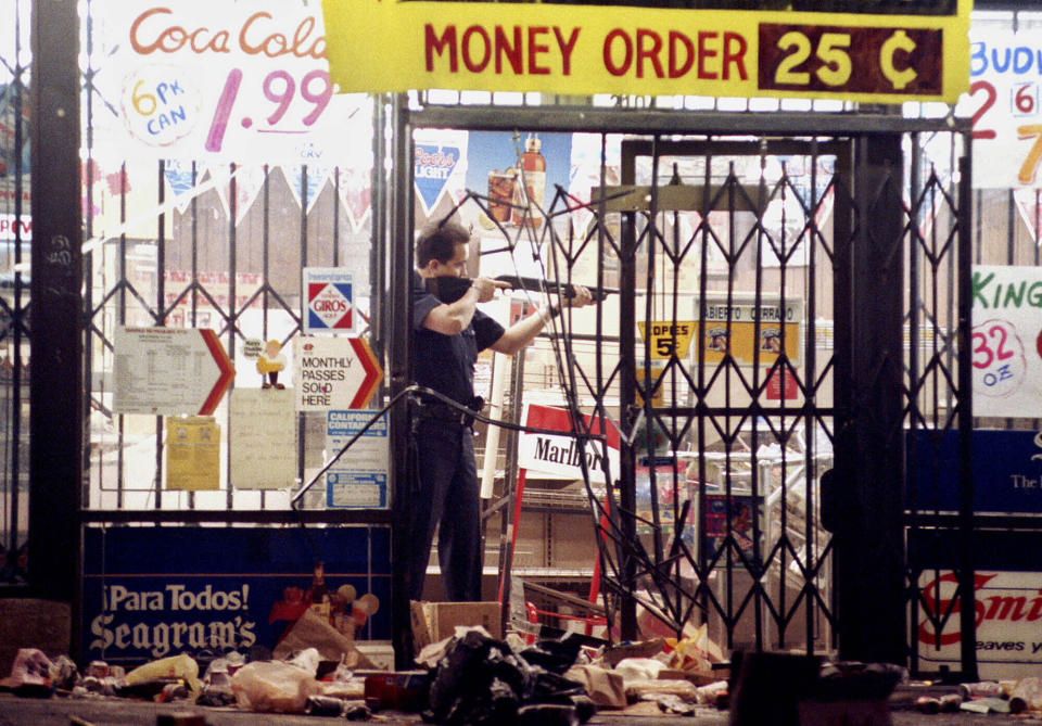 FILE - A Los Angeles police officer takes aim at a looter in a market at Alvarado and Beverly Boulevard in Los Angeles, April 30, 1992, during the second night of rioting in the city. Former award-winning Associated Press photographer John Gaps III, who documented everything from war zones to the NCAA College World Series during his career, was found dead at his home Monday, Oct. 17, 2022, in Des Moines, Iowa, his family confirmed Tuesday. He was 63. (AP Photo/John Gaps III, File)