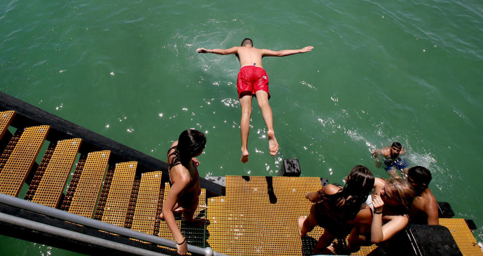 Adelaide beachgoers launch themselves from a jetty to escape the heat. Image: AAP