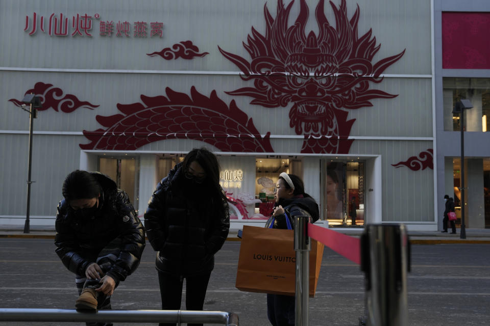 Shoppers wait for their ride near a store decorated with a dragon motif ahead of the lunar Year of the Dragon in Beijing, Monday, Jan. 22, 2024. China's central bank said Wednesday it will cut the ratio of reserve banks must hold to help boost the slowing economy. (AP Photo/Ng Han Guan)