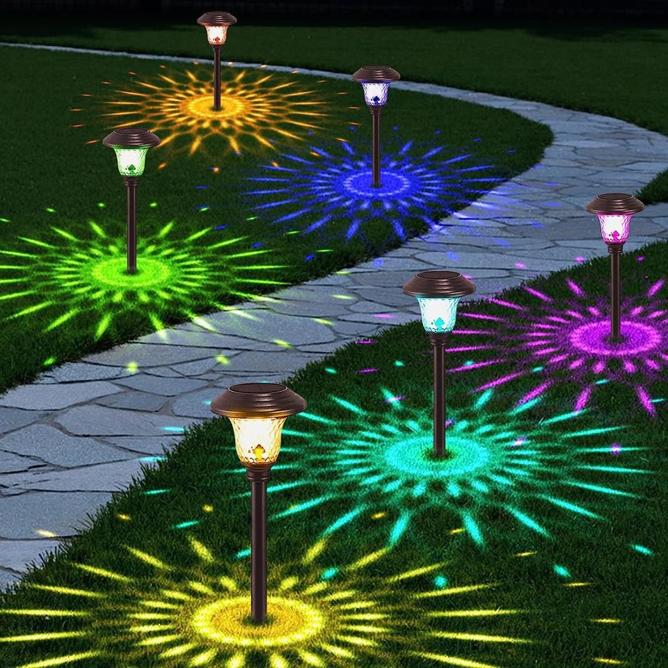 Winding stone pathway lit by multi-colored pathway lights casting patterns on the grass