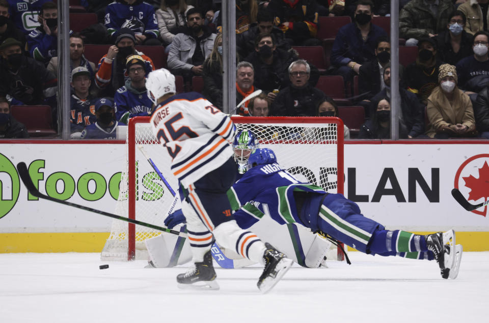 Vancouver Canucks' Matthew Highmore, right, dives to try and block Edmonton Oilers' Darnell Nurse's shot on Vancouver goalie Spencer Martin, back, during overtime in an NHL hockey game, Tuesday, Jan. 25, 2022 in Vancouver, British Columbia. (Darryl Dyck/The Canadian Press via AP)