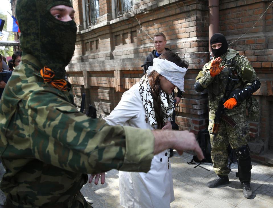 Masked pro-Russian man escorts pro-Ukrainian activist and journalist Irma Krat after she was shown to journalists in Slovyansk, eastern Ukraine, Monday, April 21, 2014, after Krat was taken captive by pro-Russian insurgents. The self-proclaimed mayor of Slovyansk in eastern Ukraine is appealing to Russia to send in peacekeeping troops after a shootout at checkpoint near the city manned by pro-Russia insurgents. (AP Photo/Sergei Grits)