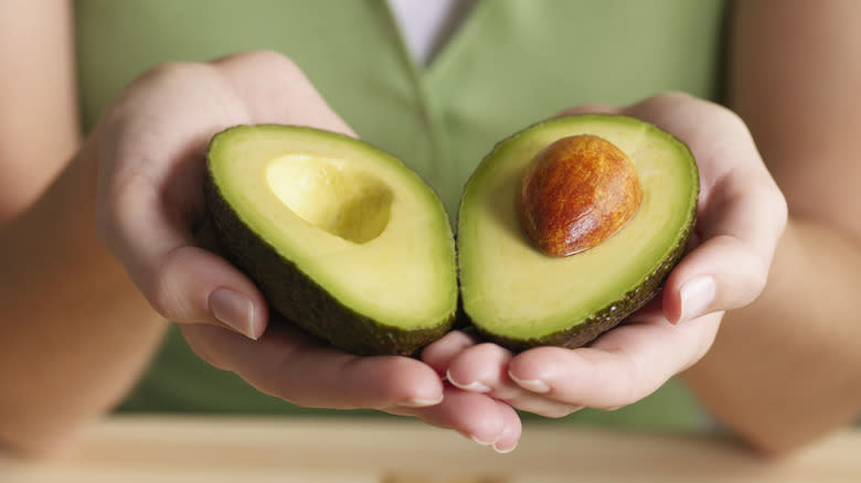 Hands holding a cut avocado