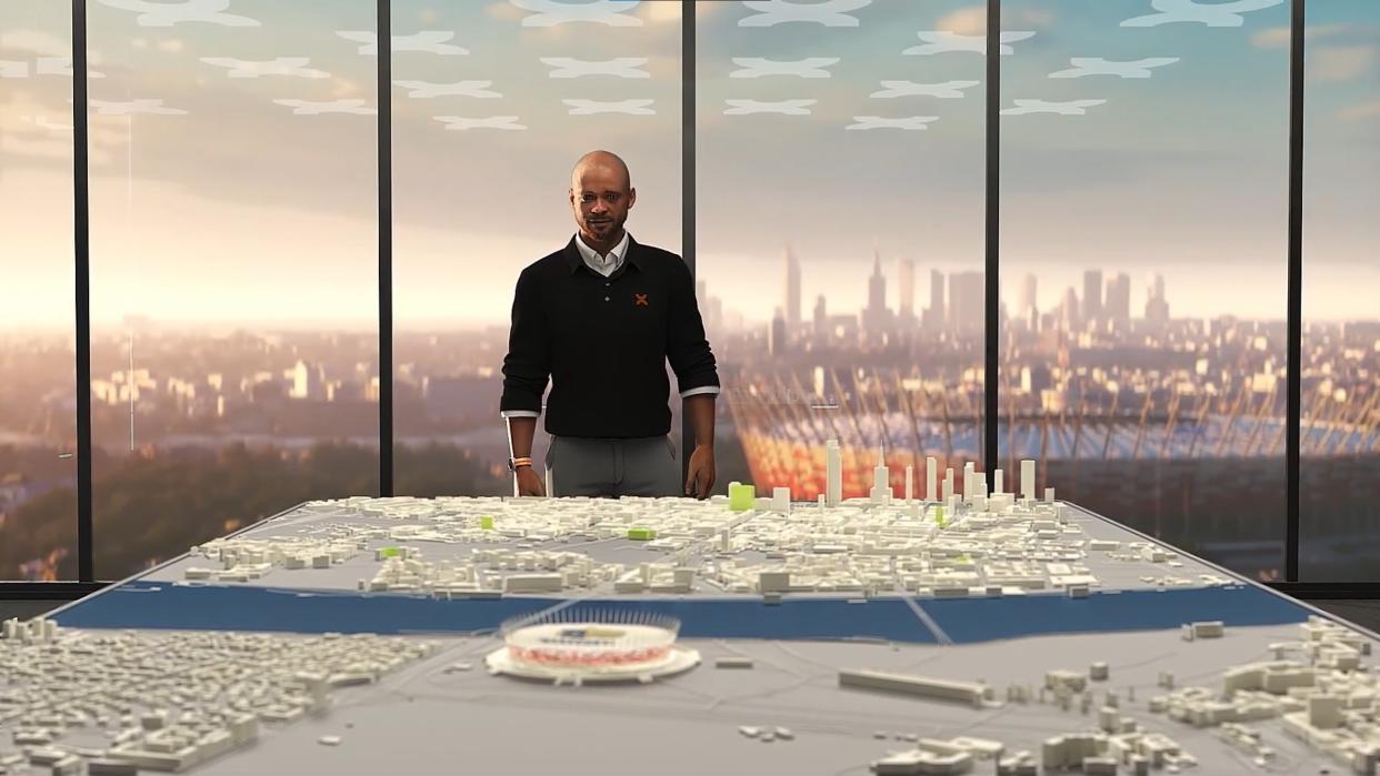  Copa City 25 - a man in a sweater stands behind a city plan diorama with a football stadium out the window. 