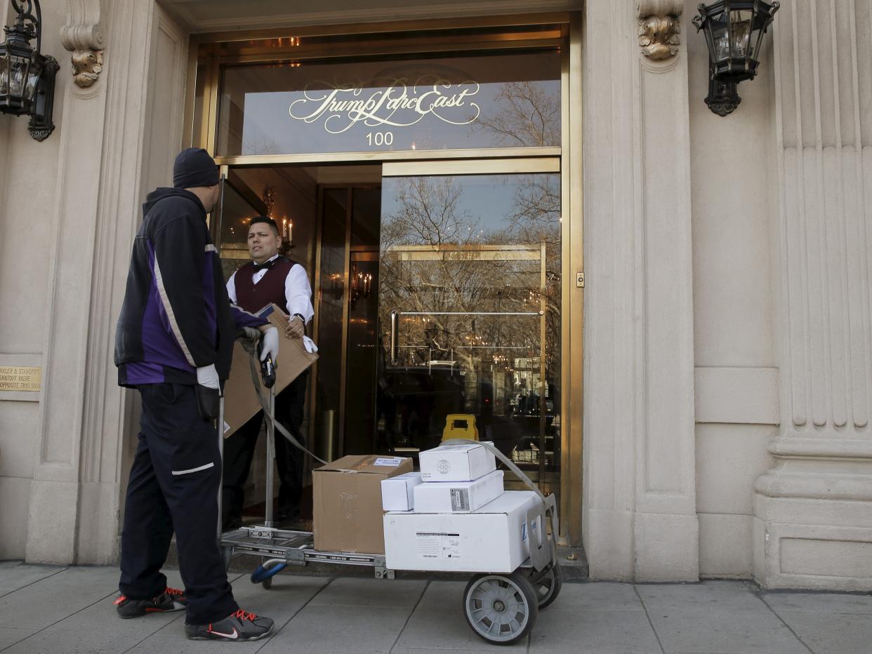 A FedEx delivery man talks to a doorman in a fancy New York City Apartment building with a gold door.