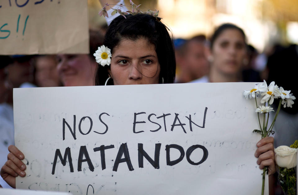 FILE - In this Feb. 20, 2014 file photo, an opposition demonstrator holds a poster that reads in Spanish "They are killing us" outside the Venezuelan Military Industries (CAVIM) in Caracas, Venezuela. For years the opposition has insisted the government is illegitimate rather than succeeding in building bridges across class lines, reinforcing perceptions that it hasn't evolved since it backed a failed 2002 coup against then President Hugo Chavez. (AP Photo/Alejandro Cegarra, File)