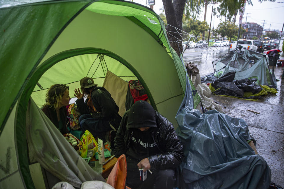 FILE - In this March 12, 2020, file photo, people try to stay warm as they face the elements inside a homeless encampment flooded under a rainstorm across the Echo Park Lake in Los Angeles. Faced with an out-of-control homeless crisis, On Monday, April 19, 2021, Los Angeles Mayor Eric Garcetti announced plans to spend nearly $1 billion in the coming year in hopes of getting tens of thousands of unhoused people off the streets. (AP Photo/Damian Dovarganes, File)