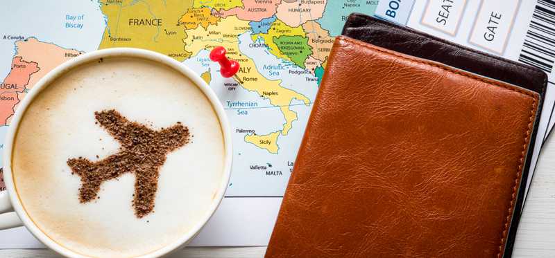 A travel airplane in a cappuccino on top of a map,tickets, and passport book.