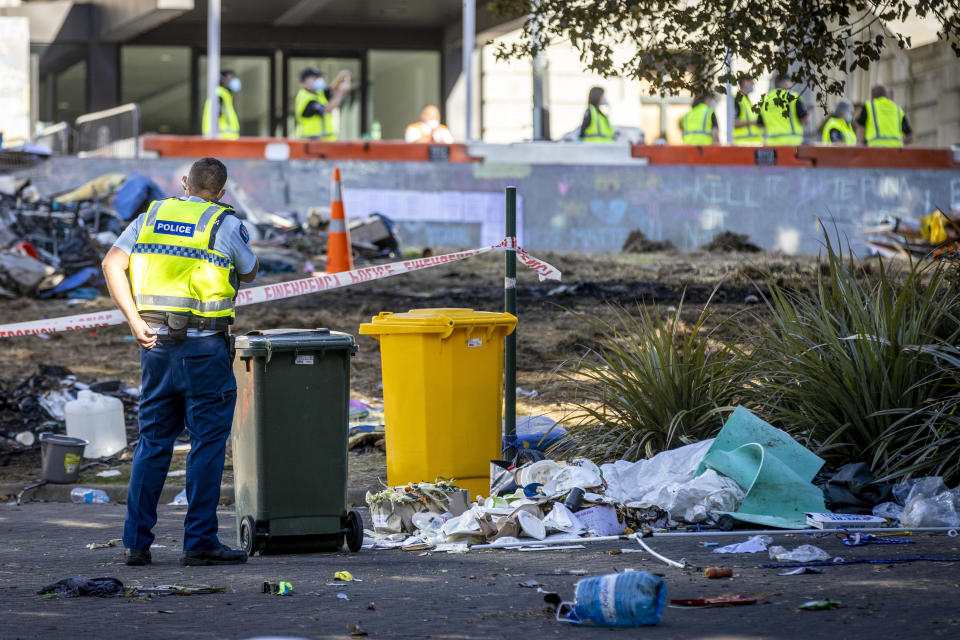 A policeman stands as work begins to clean up the grounds outside Parliament following Wednesday's violent end to protests opposing coronavirus vaccine mandates in Wellington, New Zealand, Thursday, March 3, 2022. Since the beginning of the pandemic, New Zealand has reported fewer than 100 virus deaths among its population of 5 million, after it imposed strict border controls and lockdowns to eliminate earlier outbreaks. (Mike Scott/New Zealand Herald via AP)