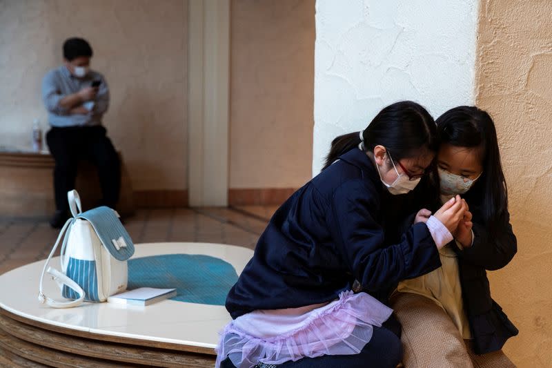 Children wearing face masks, following an outbreak of the coronavirus, use a mobile phone at a mall in Tokyo