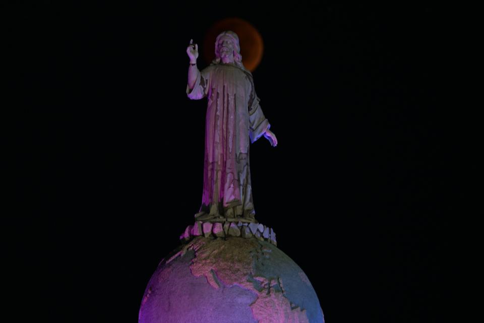The blood moon is seen during a total lunar eclipse past the Savior of the World monument in Salvador del Mundo Square, in San Salvador on November 8, 2022.